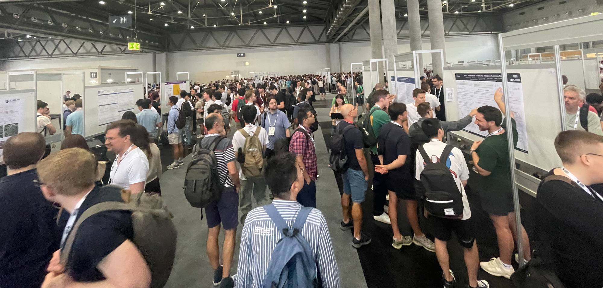 Interior of a bustling academic conference hall with many attendees, some carrying backpacks, and research posters displayed 